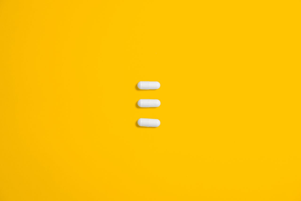 hero-img-01 White pills arranged on a vibrant yellow background, emphasizing simplicity and healthcare.